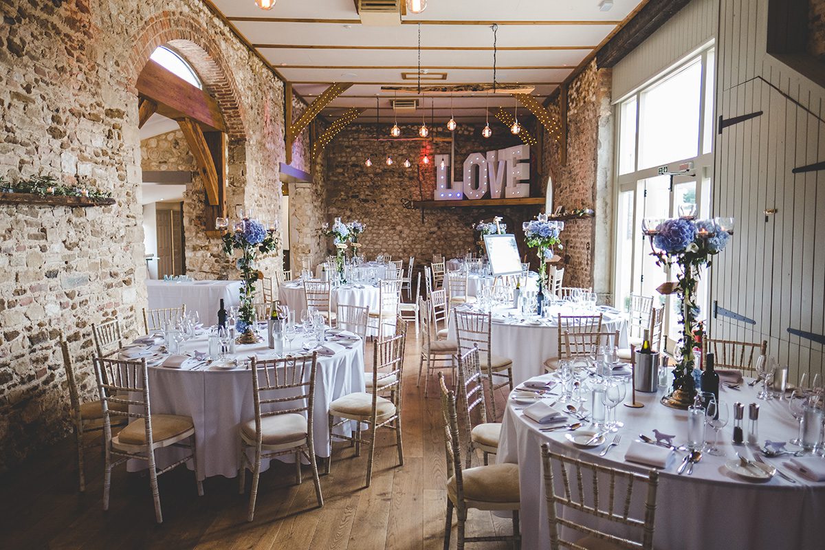 The barn was set up for the breakfast with vases of pretty blue wedding flowers as table centrepieces at Pentney Abbey